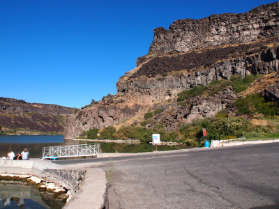 [A paved area leads to a dock in the waters just behind the dam. One is in the canyon in this area and the walls of it form large 